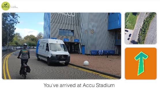 Screenshot from Huddersfield Railway Station to Accu Stadium cycle route video showing a woman on a bike in front of the Accu Stadium