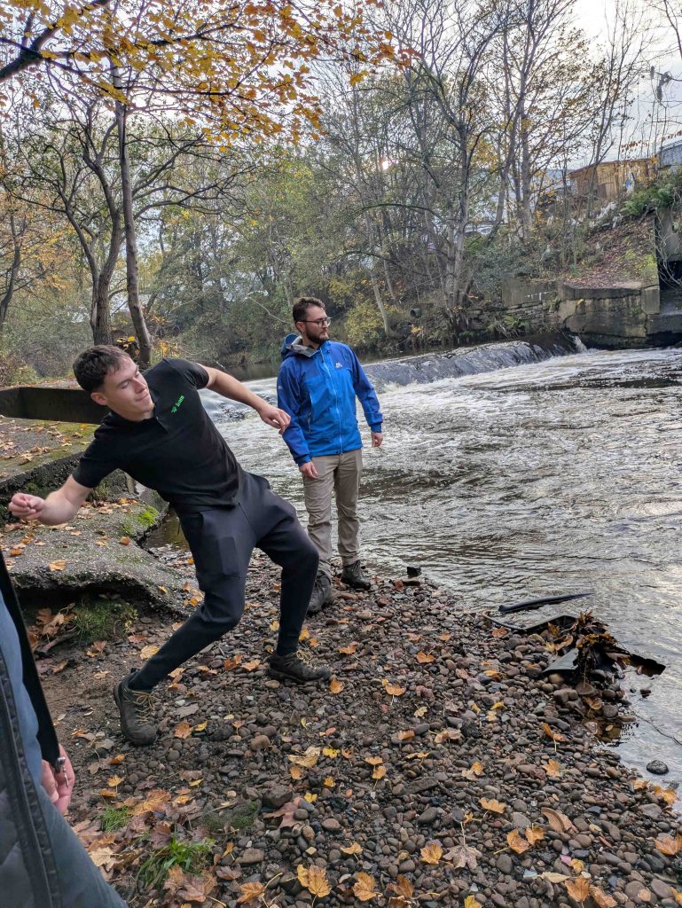 Image of man skipping stones next to the riverside in Huddersfield Riverside Nature Park as his colleague watches